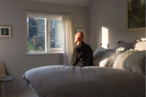 Older man sitting on bed looking out of window